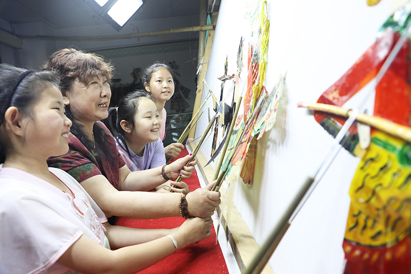 皮影藝人指導(dǎo)小朋友表演皮影戲。