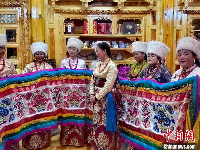 圖為女性展示村民自發(fā)繡制的“百米五彩哈達(dá)”?！±钣穹?攝